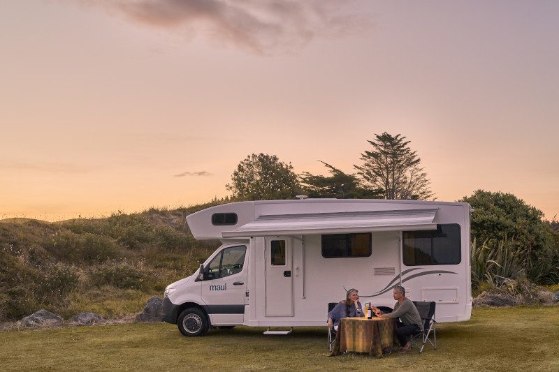 Couple-relaxing-by-motorhome-at-sunset